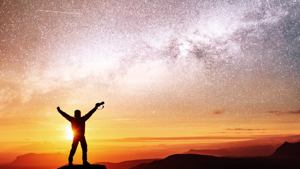 Silhouette of woman is standing on top of mountain and pointing to The milky way before sunrise and enjoying with colorful night sky.