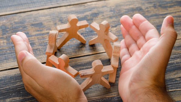 Business success concept on wooden background high angle view. hands protecting wooden figures of people.
